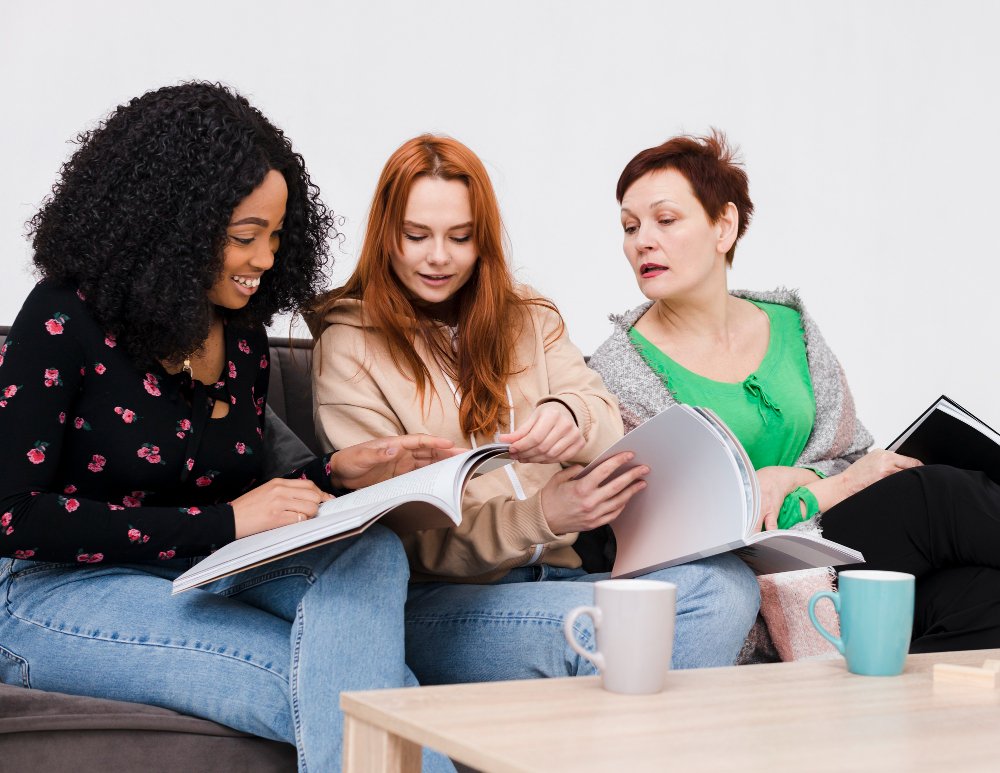 Tres mujeres sentadas juntas leyendo y compartiendo un libro.